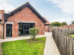 A brick building with a large window, a small garden, and a wooden fence.