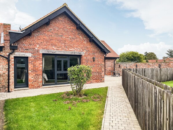 A brick building with a large window, a small garden, and a wooden fence.