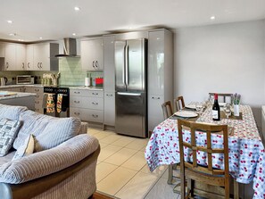 A modern kitchen with stainless steel appliances, a dining area with a table set for two, and a cozy seating area with a patterned sofa. - Barn Owl Cottage - UK48510 (Kirk Hammerton, near York)