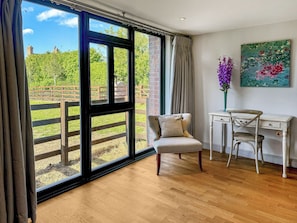A room with a large window, a desk, a chair, and a painting on the wall.