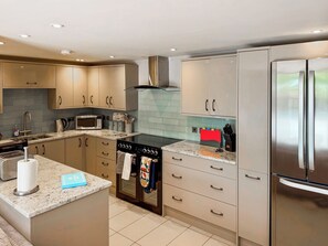 A modern kitchen with stainless steel appliances, beige cabinetry, and a tiled backsplash.