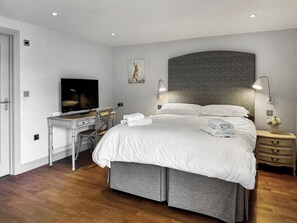 A modern hotel room with a large bed, a desk with a flat-screen TV, a wall-mounted lamp, and a small bedside table with a vase of flowers. - Barn Owl Cottage - UK48510 (Kirk Hammerton, near York)