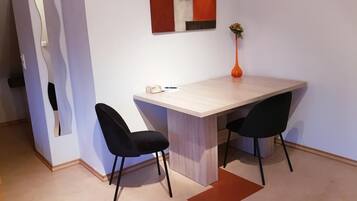 Ein kleiner, moderner Raum mit einem Holztisch und zwei schwarzen Stühlen. Auf dem Tisch steht eine Vase mit Blumen, an der Wand ein Spiegel.