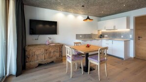 Una cocina moderna con armarios blancos, una mesa de comedor de madera y un televisor montado en la pared.