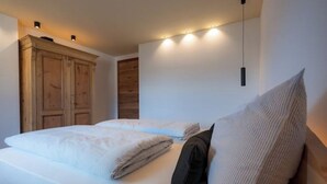 Un dormitorio con cama, almohadas, un armario de madera e iluminación en la pared.