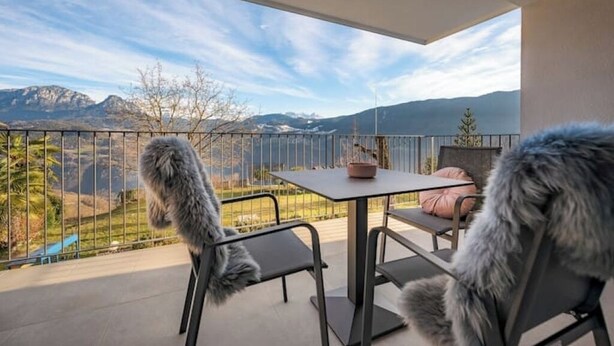 Un balcón con mesa y sillas, con vista a un paisaje montañoso.