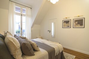 A bedroom with a bed, a window with curtains, a door, and two framed pictures on the wall. - Balcon Champs Elysees (Paris)