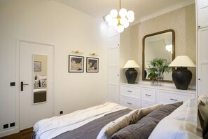A bedroom with a bed, bedside tables, a dresser, a mirror, and wall-mounted lights. - Balcon Champs Elysees (Paris)