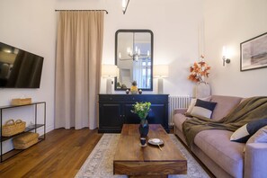 Un salon avec un canapé, une table basse, un téléviseur, un miroir et un vase rempli de fleurs.