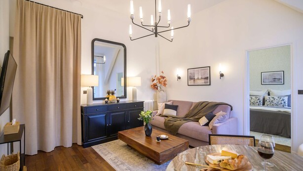A living room with a sofa, a coffee table, a dining table with food and drink, a chandelier, and a large mirror. - Balcon Champs Elysees (Paris)