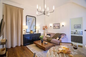 A living room with a sofa, a coffee table, a dining table with food and drink, a chandelier, and a large mirror. - Balcon Champs Elysees (Paris)