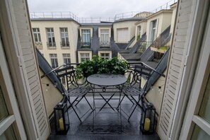 A small outdoor balcony with a metal table and chairs, surrounded by buildings. - Balcon Champs Elysees (Paris)