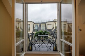 A balcony with a table and chairs, a potted plant, and a view of neighboring buildings.