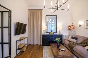 A modern living room with a flat-screen TV, a dark wooden coffee table, a beige sofa, and a black console table with decorative items. - Balcon Champs Elysees (Paris)