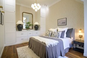 A bedroom with a bed, bedside lamps, a nightstand, a mirror, and a dresser.