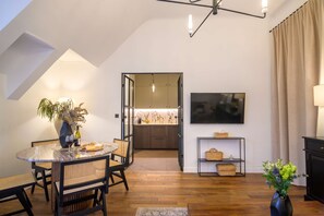 A modern living room with a dining area, a kitchen visible through an open door, a flat-screen TV mounted on the wall, and a small shelf with baskets. - Balcon Champs Elysees (Paris)