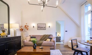 A modern living room with a sofa, coffee table, and a dining area with a chair and table. - Balcon Champs Elysees (Paris)