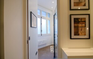 A hallway with a door leading to a room, a window with a view, and framed pictures on the wall.