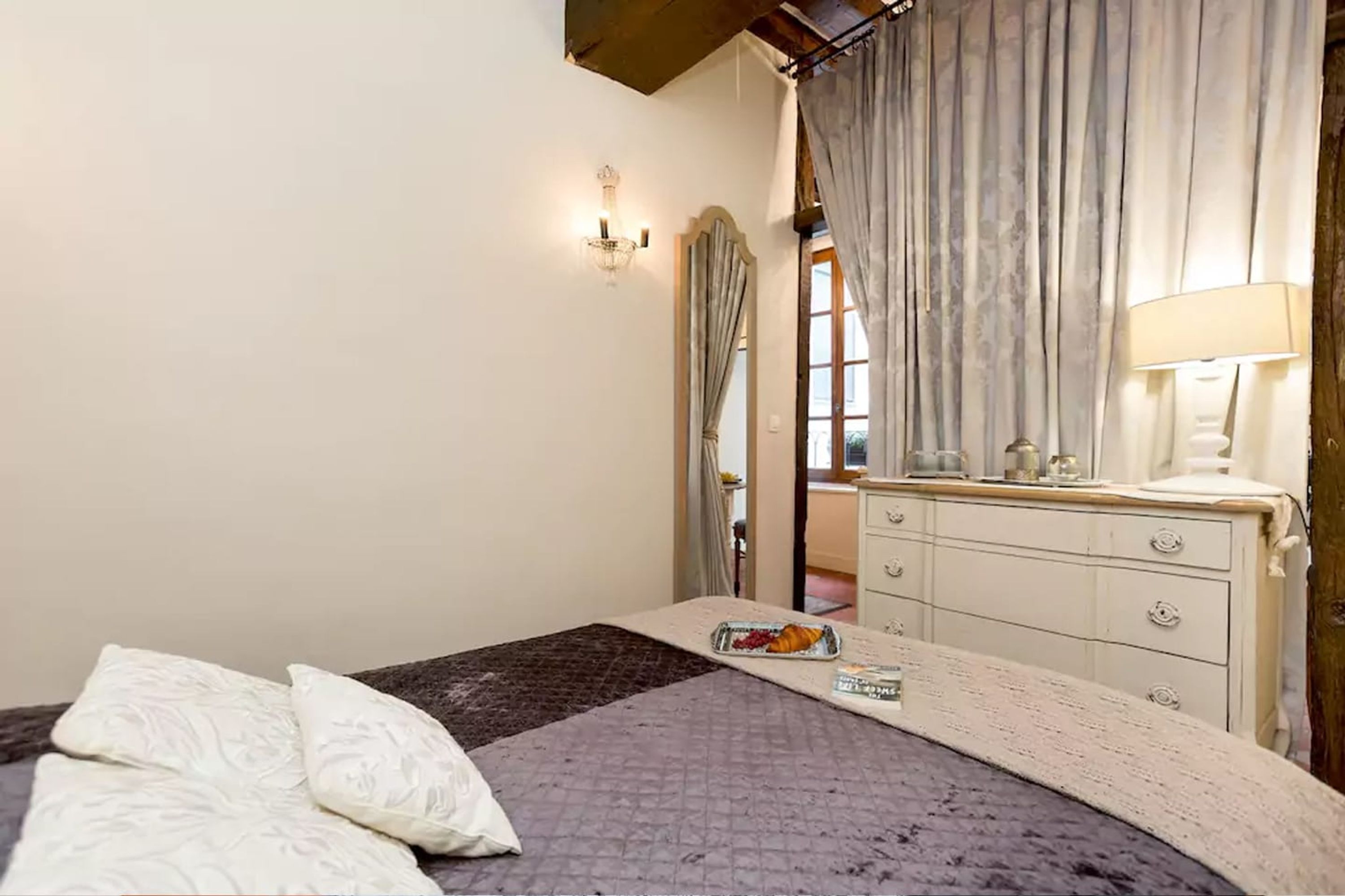 A bedroom with a bed, a dresser, a mirror, and a window with curtains.