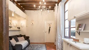 A cozy room with a dark sofa, a patterned rug, a chandelier, a white door, and a small table with a cake. - Le Diamant En Isle - Ile Saint Louis (Paris)