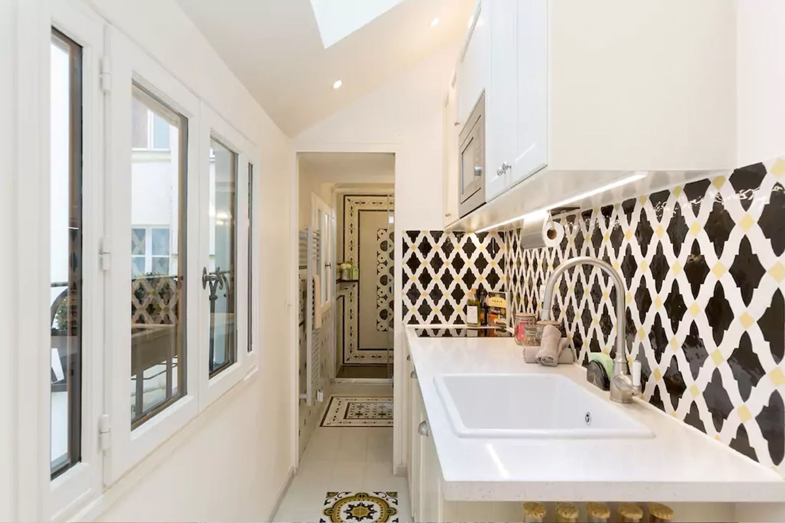 A narrow kitchen with white cabinets, a white sink, and a patterned backsplash.
