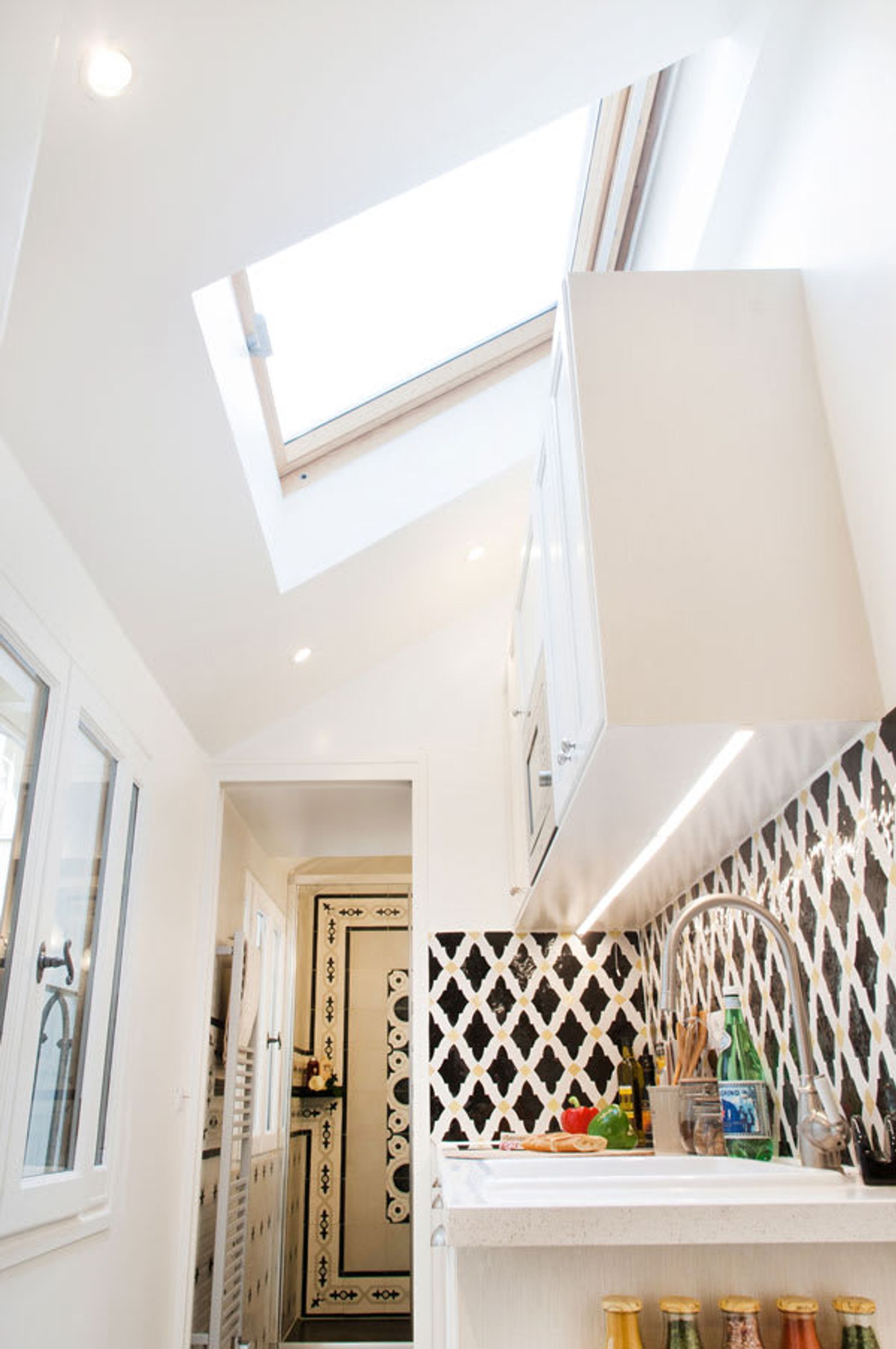 A modern kitchen with a skylight, white cabinets, a patterned backsplash, and a countertop with various items.