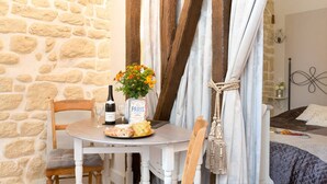 A rustic room with a stone wall, a wooden table with a bottle of wine, a plate of food, and a vase of flowers. - Le Diamant En Isle - Ile Saint Louis (Paris)