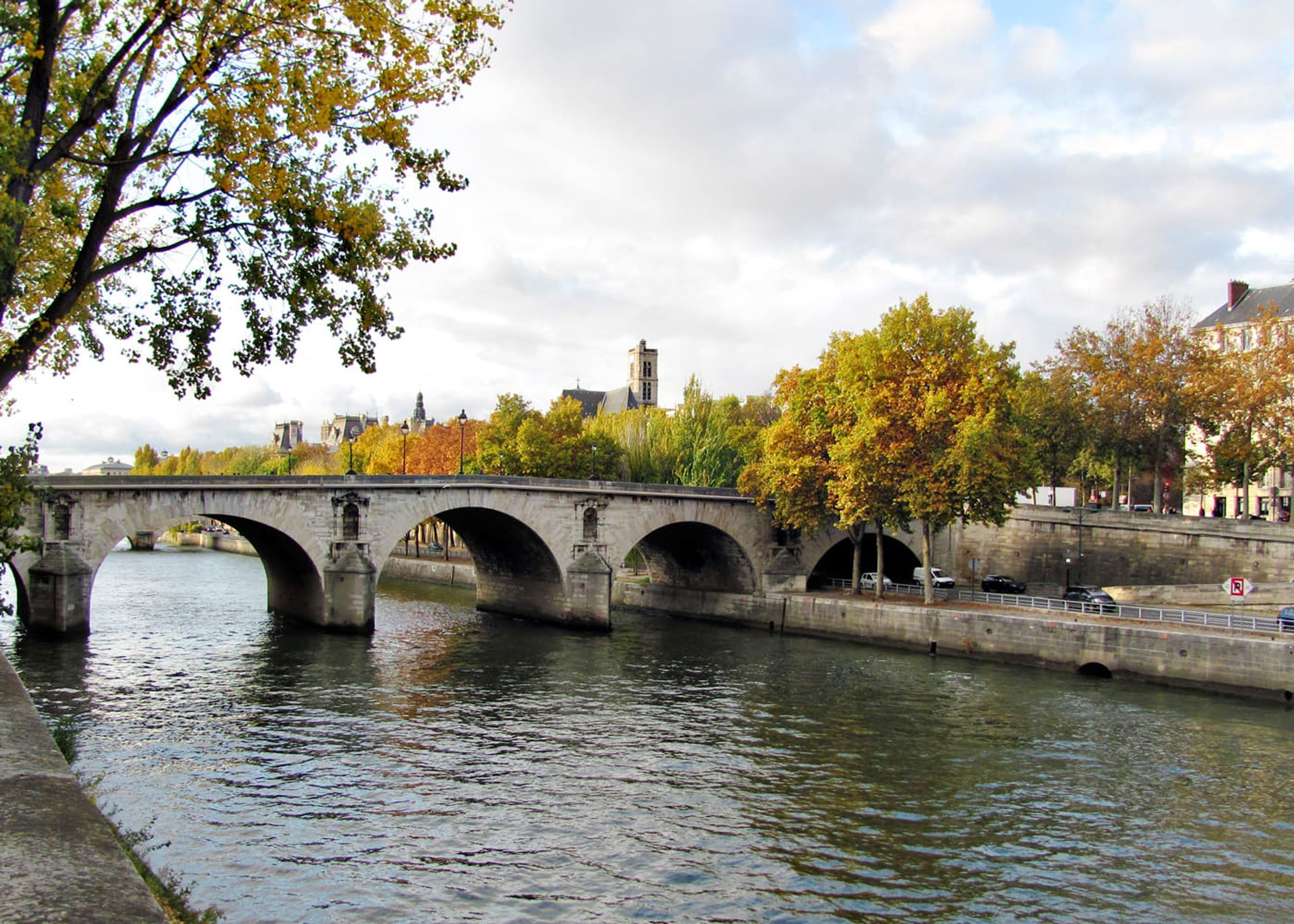 A stone bridge over a river with autumn foliage, a pedestrian path, and a no-parking sign.
