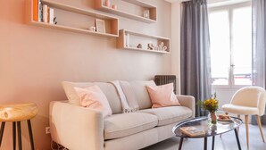 A living room with a sofa, a coffee table, a chair, and bookshelves. - Le Gourmet du Marais (Paris)