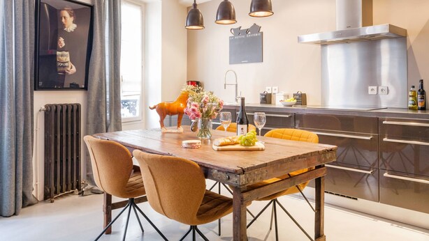 A modern kitchen with a wooden table, chairs, and a decorative pig statue. - Le Gourmet du Marais (Paris)