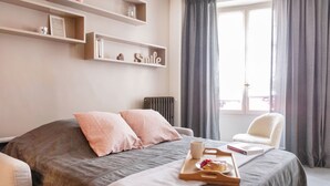 A bedroom with a bed, a chair, a tray with pastries, and shelves with decorative items. - Le Gourmet du Marais (Paris)