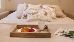Ein ordentlich bezogenes Bett mit Tablett, Gebäck und Tasse, ein gerahmtes Bild an der Wand und zwei Wandlampen.