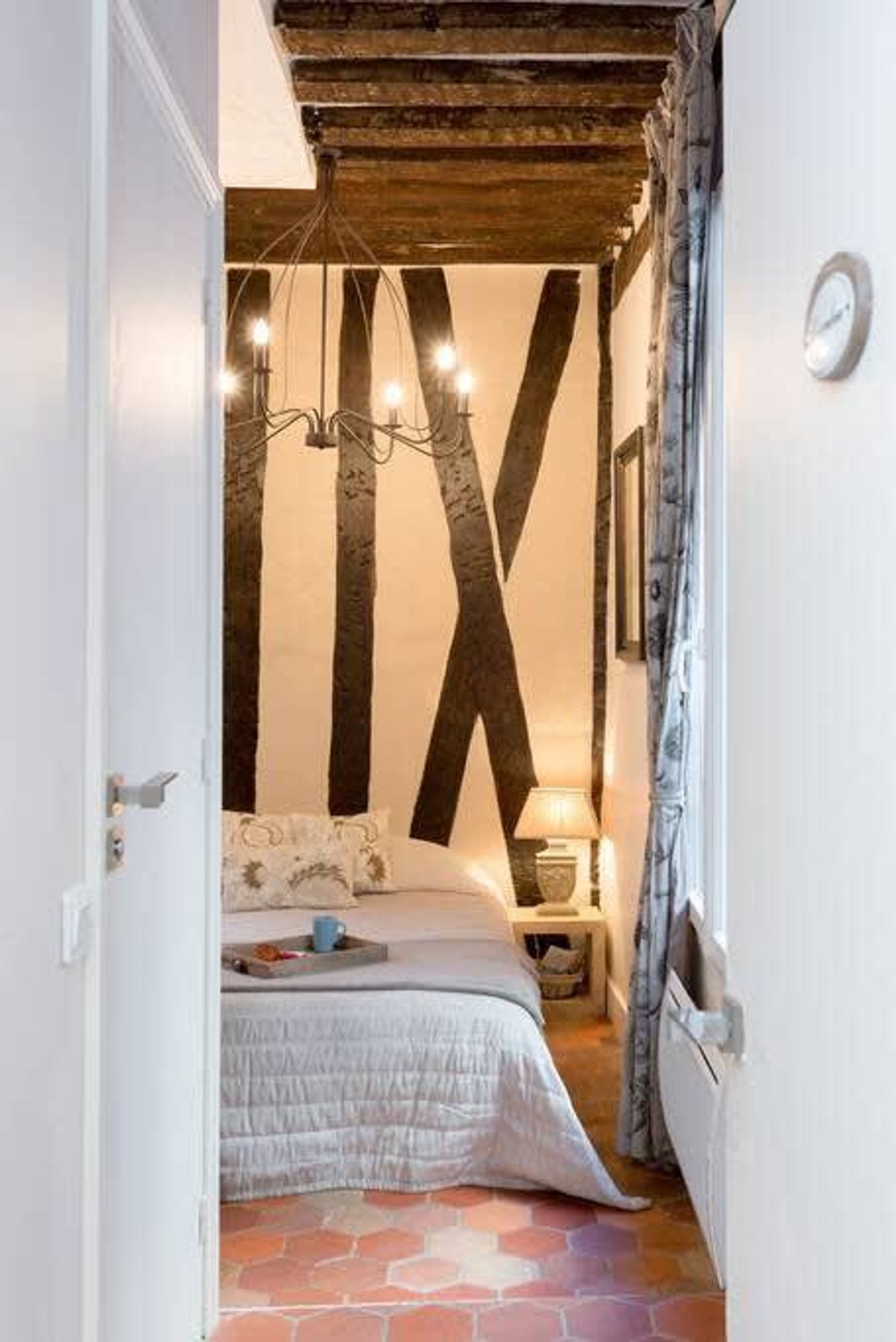 Une pièce étroite avec un lit, un lustre et une grande poutre en bois en forme de X sur le mur.