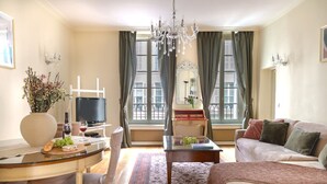 A well-lit living room with a sofa, a coffee table, a TV, and a dining area with a table and chairs. - La Lumiere Eiffel Walk to Tower (Paris)