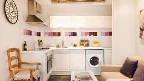 A compact kitchen with a washing machine, a dining table, and a chair.