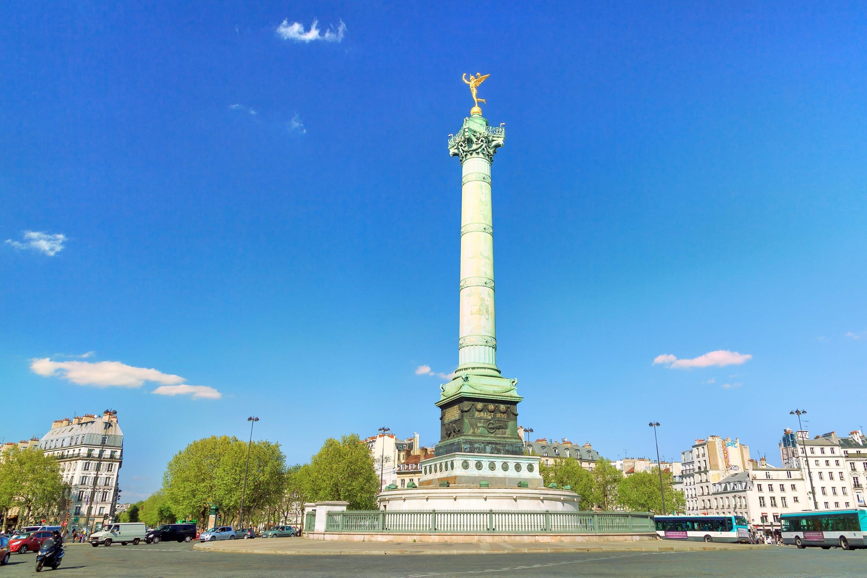 A tall monument with a statue on top, surrounded by a circular base and a fence.