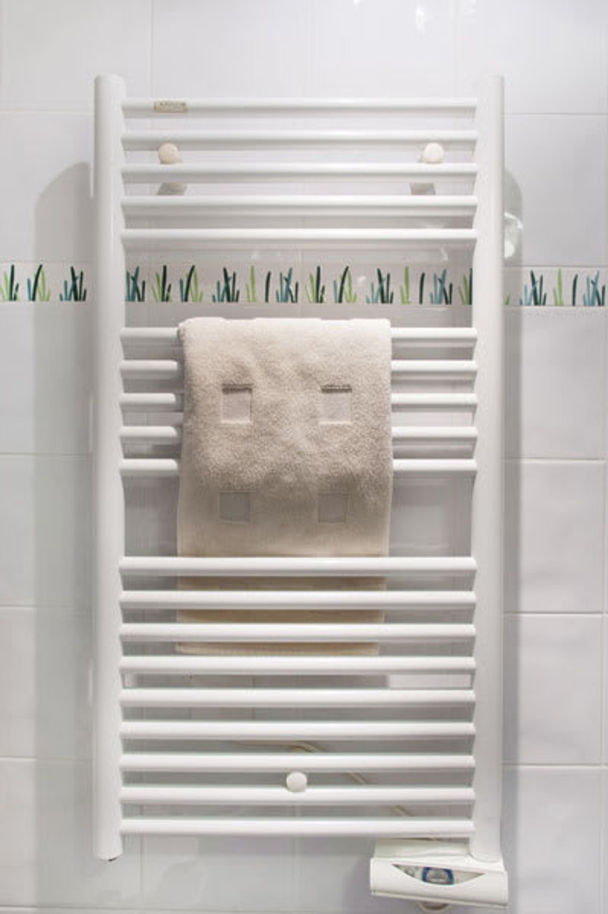 A white towel rack with a towel hanging on it, set against a tiled wall with a cactus pattern.