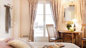 A hotel room with a bed, a dining table with chairs, a mirror, and a window with curtains.