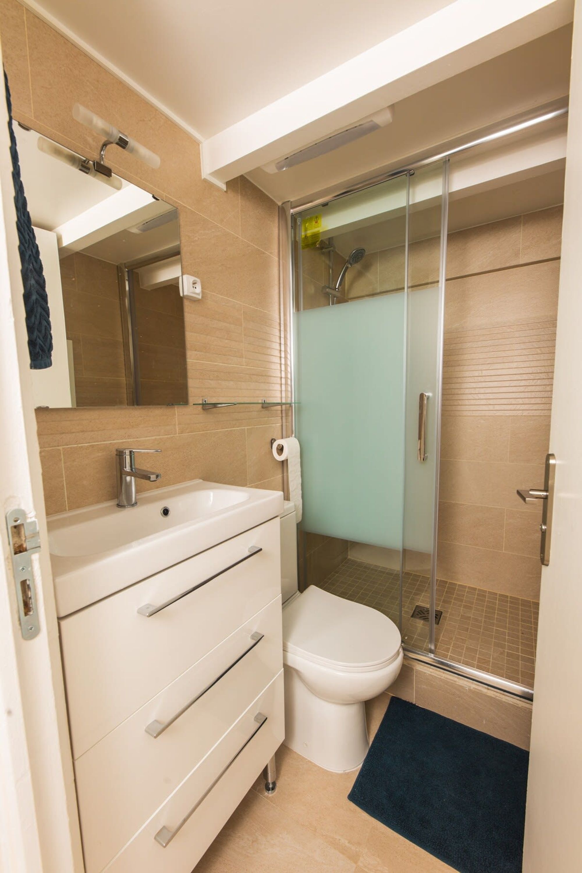 A modern bathroom with a white vanity, a glass shower enclosure, and a beige tiled floor.