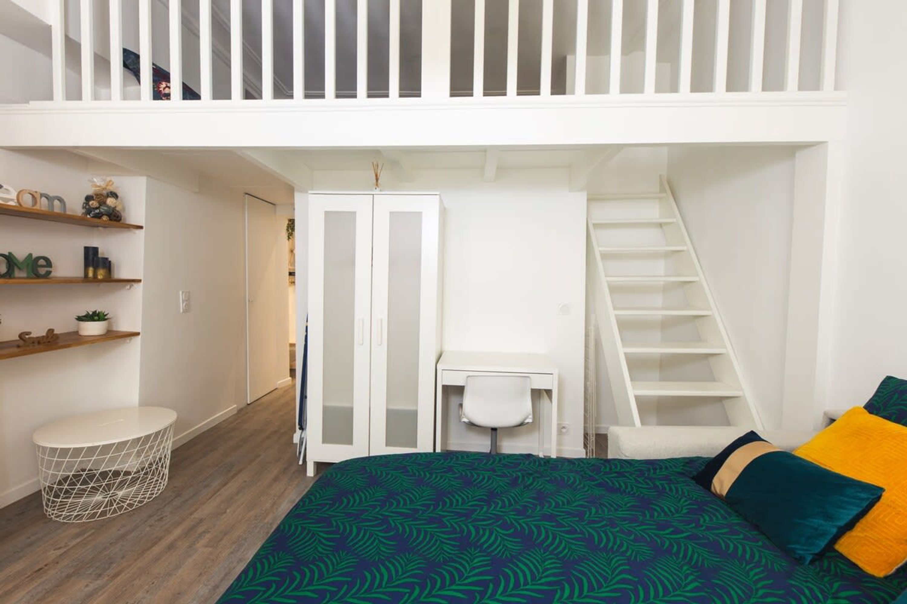 A bedroom with a bed, a desk, a chair, a wardrobe, and a staircase.