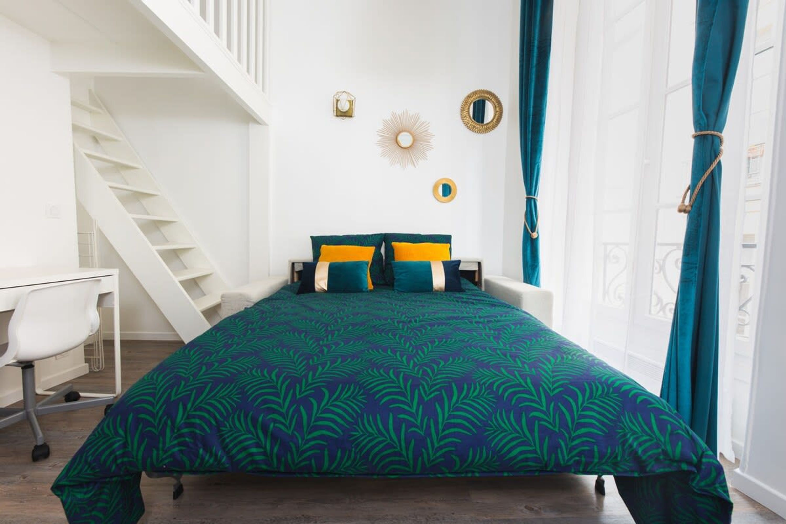 A bedroom with a bed, a desk, and a staircase.