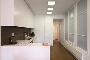 A modern kitchen with white cabinetry, a central island, and a view into a hallway with frosted glass doors. - Le Balcon de Notre Dame (Paris)