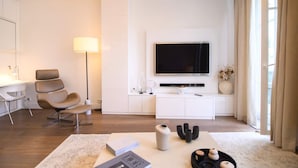 A modern living room with a flat-screen TV, a sofa, a desk, and a lamp. - Le Balcon de Notre Dame (Paris)