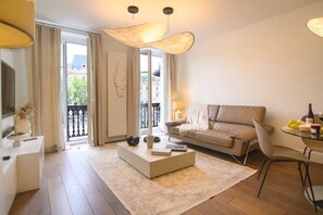 Un salon moderne avec un canapé, une table basse et un coin repas. Il y a un balcon d’où l’on peut admirer les bâtiments et les arbres.