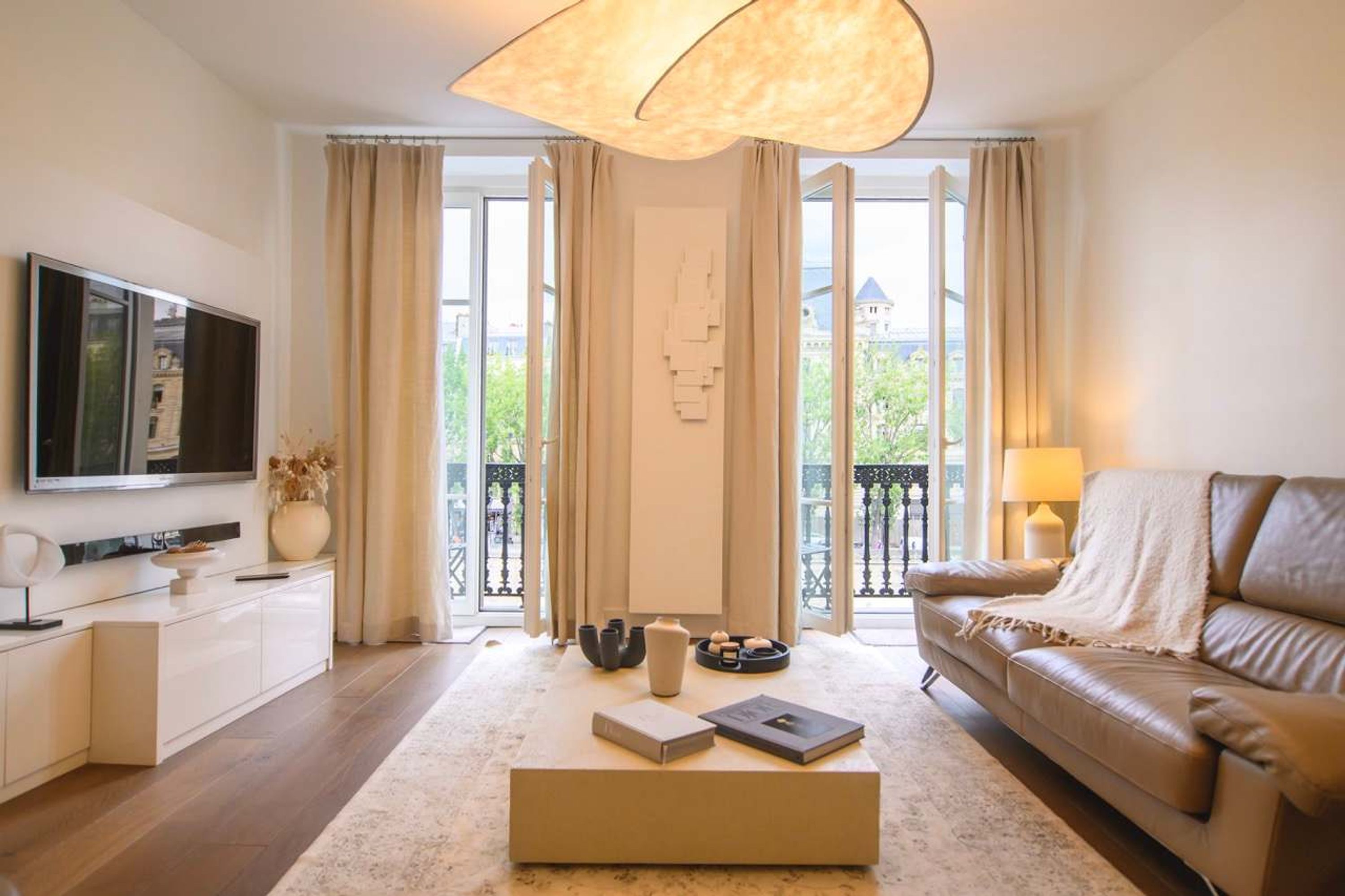 A modern living room with a sofa, a coffee table, a TV, and a balcony with curtains.
