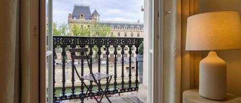 Ein Zimmer mit Blick auf ein historisches Gebäude gegenüber einem Kanal, ein Balkon mit einem Stuhl und eine Lampe auf einem Nachttisch.