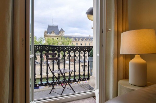 A room with a view of a historic building across a canal, a balcony with a chair, and a lamp on a bedside table. - Le Balcon de Notre Dame (Paris)