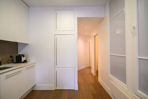 A compact kitchen with white cabinetry and a wooden floor. - Le Balcon de Notre Dame (Paris)