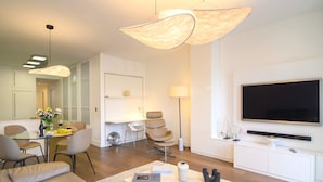 A modern living room with a flat-screen TV, a dining area with a glass table, and a kitchen with white cabinets. - Le Balcon de Notre Dame (Paris)
