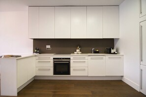 A modern kitchen with white cabinetry, a built-in oven, and a coffee machine. - Le Balcon de Notre Dame (Paris)